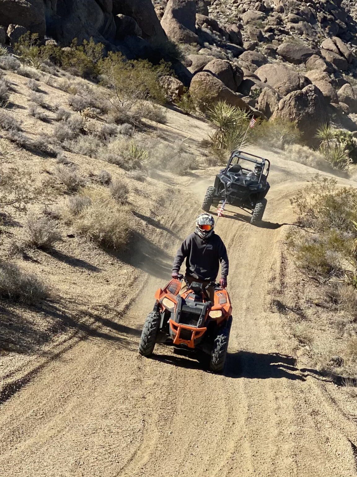 Two people on four wheelers driving down a dirt road.